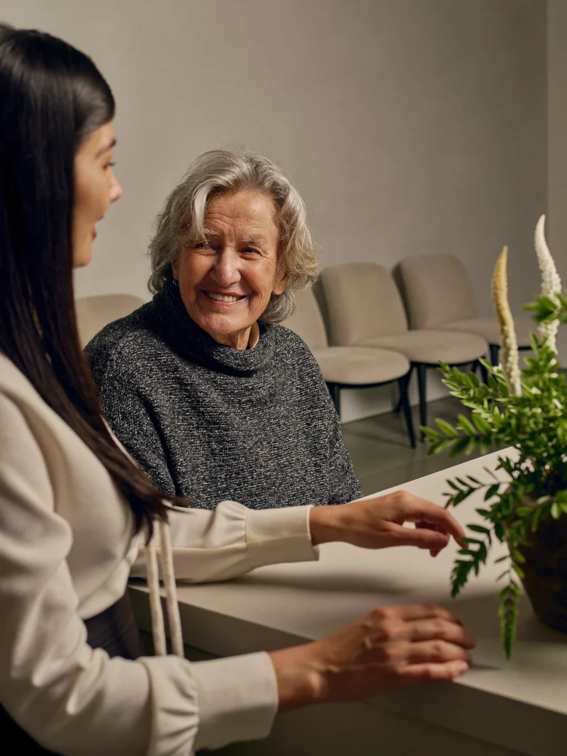Senior spricht an einem schlichten Servicetresen mit einer Mitarbeiterin, als Illustration.