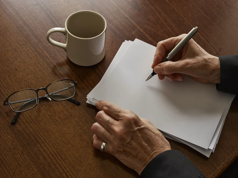 Hände mit Stift über leeren Formularen neben Lesebrille und Tasse, als Illustration.